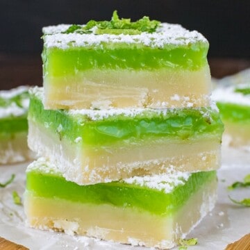 A stack of three key lime shortbread bars stacked on a wooden cutting board.