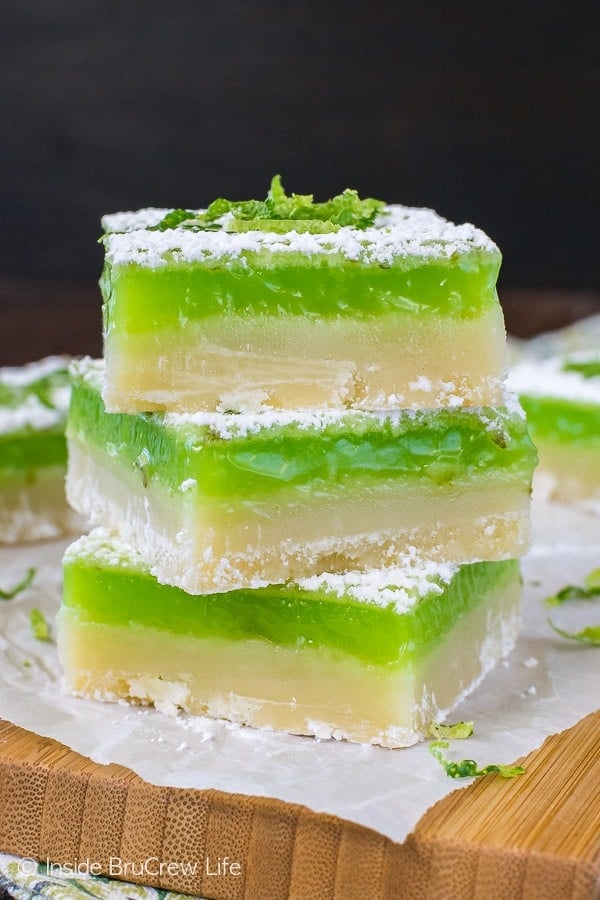 Three shortbread cookie bars with key lime filling stacked on a wooden cutting board.