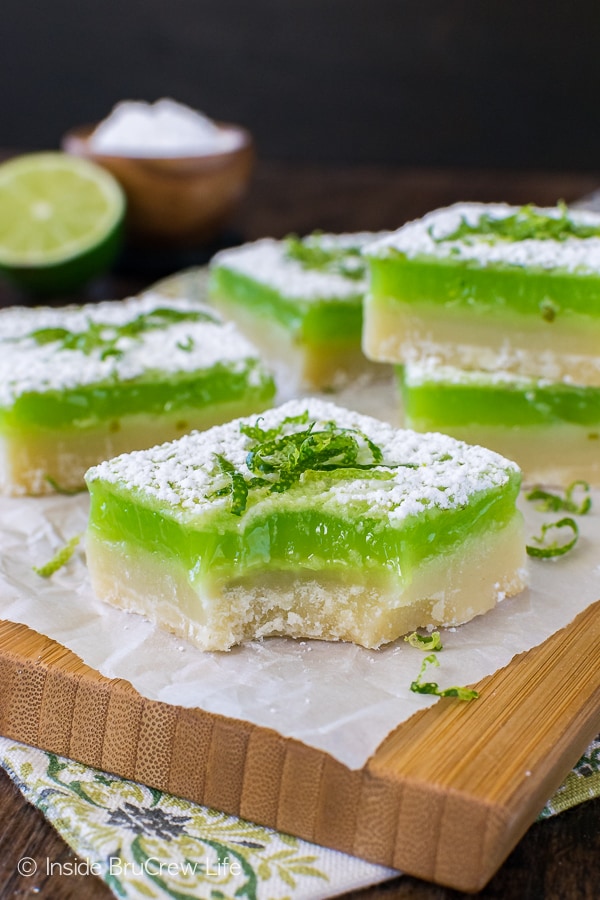 Key lime shortbread bars stacked on a wooden cutting board topped with powdered sugar and key lime zest.