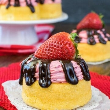 A strawberry mousse cake with chocolate drizzles and a strawberry on a white and red towel.