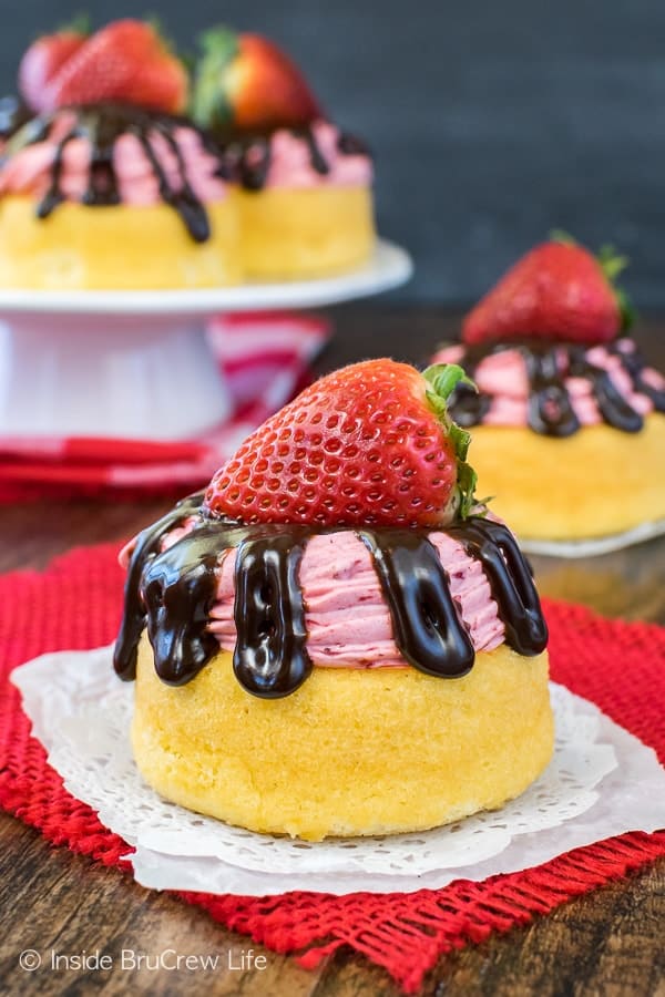 A strawberry mousse cake topped with hot fudge drizzles and a fresh strawberry on a red towel.