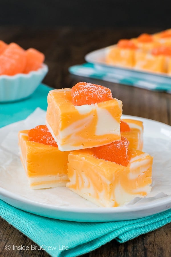 A white plate with a few squares of orange creamsicle fudge stacked on it.