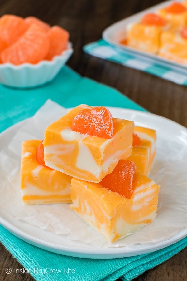 Four pieces of orange fudge stacked up on a white plate.