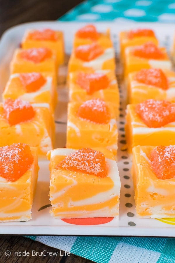 A white tray filled with orange creamsicle fudge squares topped with an orange jelly candy