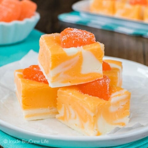 A stack of orange fudge on a white plate with more fudge behind it