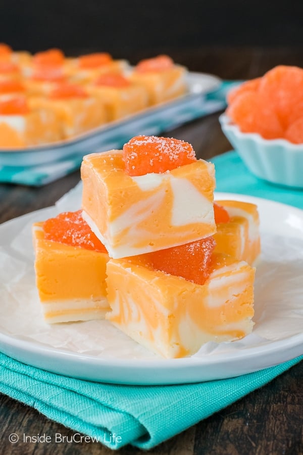 A white plate with a few squares of orange creamsicle fudge stacked on it