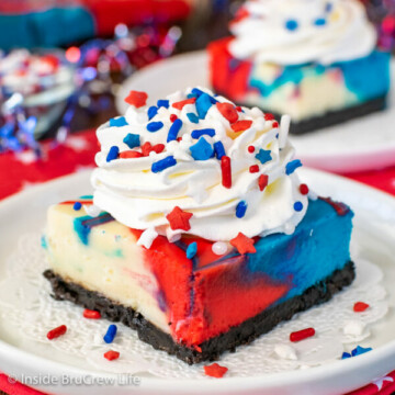 A white plate with a square of red white and blue cheesecake bars with whipped cream and sprinkles on it