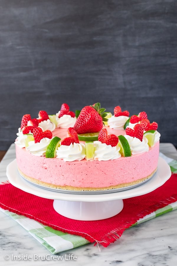 A white cake plate with a decorated strawberry mousse cake sitting on it.