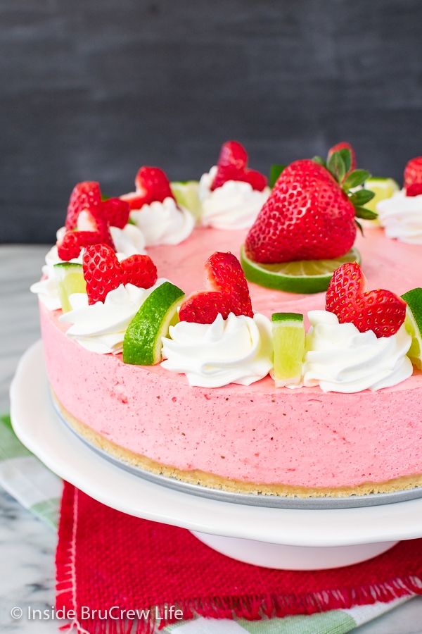 A close up of the side of a pink cheesecake topped with strawberries.