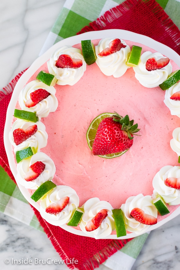 Overhead picture of a pink cheesecake topped with strawberries and lime wedges.