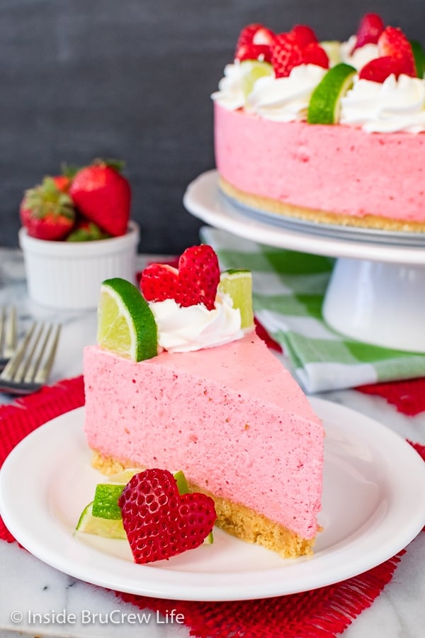 A white plate with a slice of pink cheesecake on it.