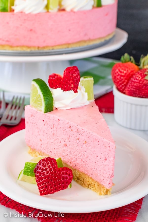 A white plate with a slice of pink strawberry cheesecake on it.