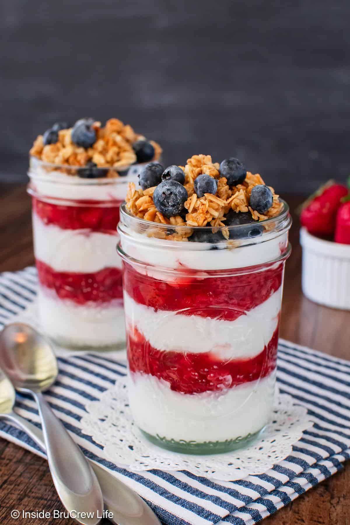 Two strawberry yogurt parfaits topped with granola and fresh blueberries.
