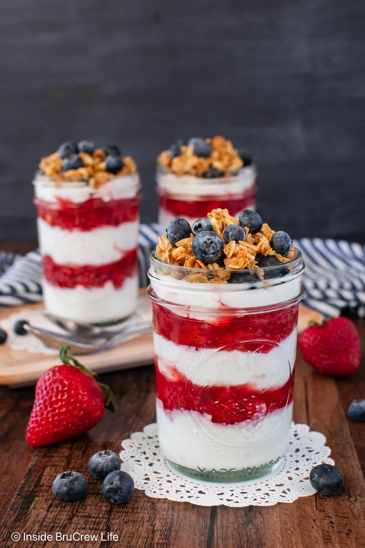 Three yogurt parfaits with layers of strawberry sauce in between the yogurt.