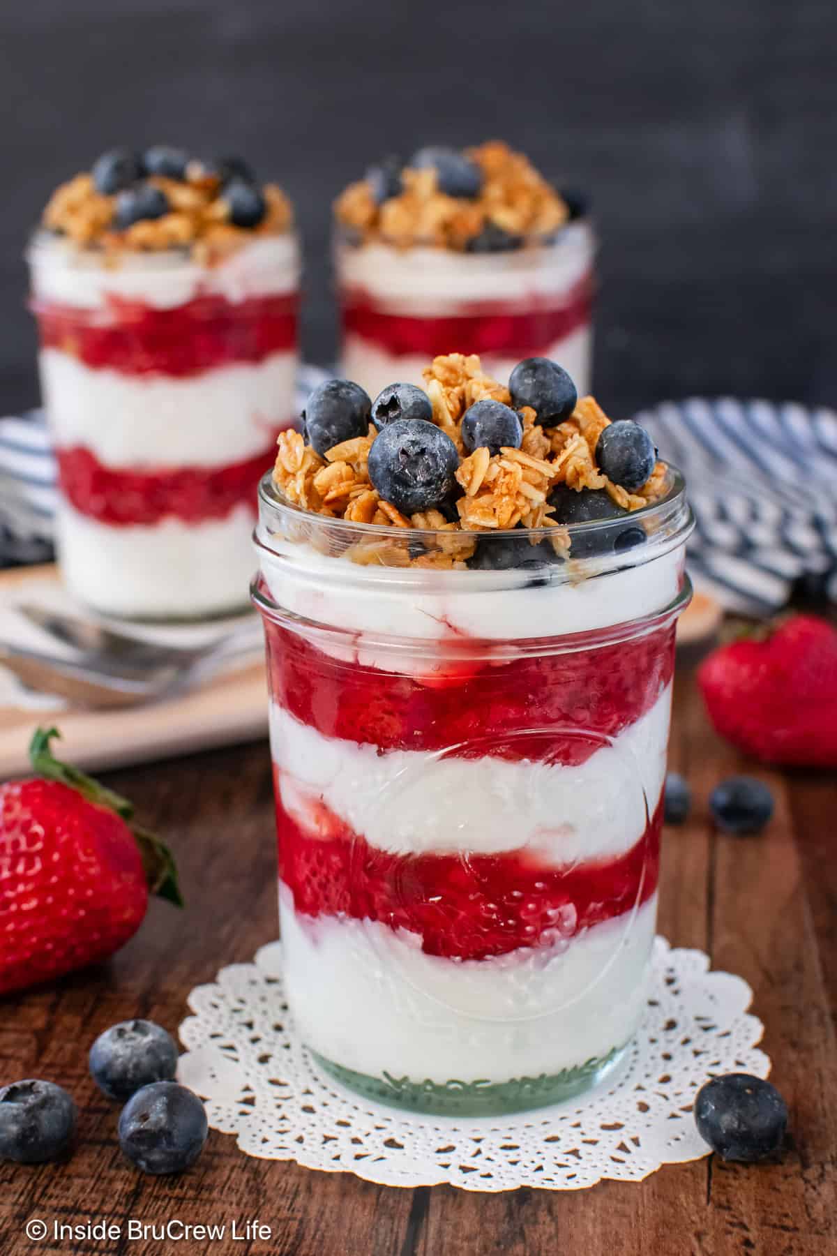 Three yogurt parfaits with layers of strawberry sauce in between the yogurt.