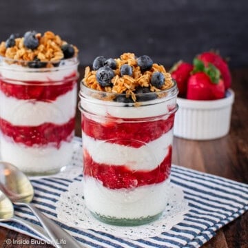 Two strawberry yogurt parfaits filled with layers of Greek yogurt and homemade strawberry sauce.