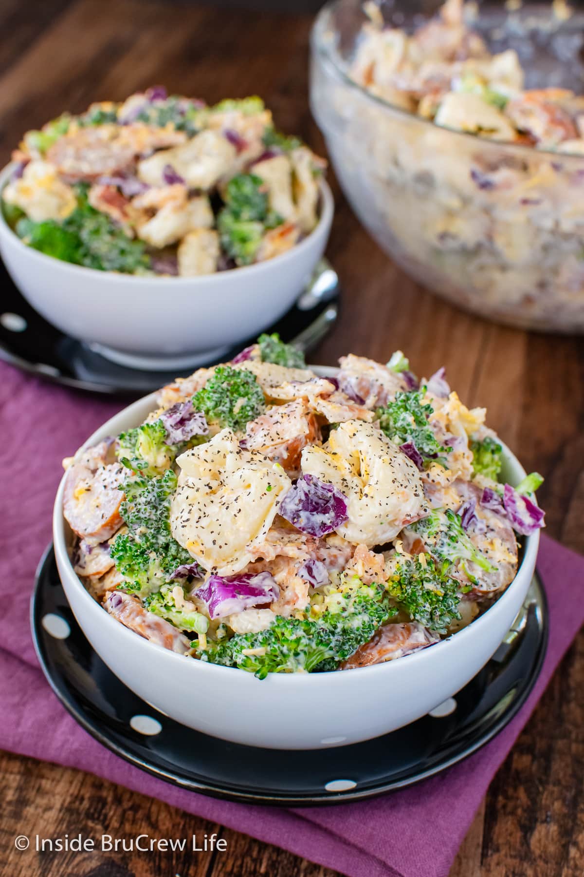 Two white bowls filled with a creamy pasta salad with veggies.