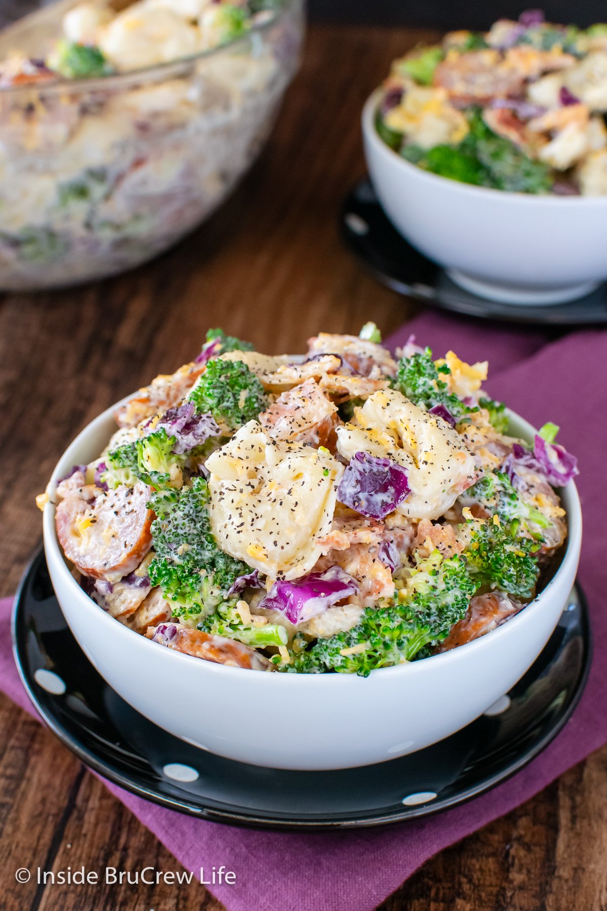 Two white bowls filled with a creamy pasta salad with veggies.