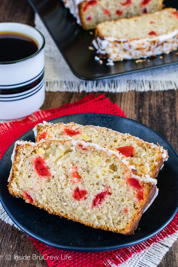 Two slices of tropical banana bread on a black plate with a cup of coffee beside them