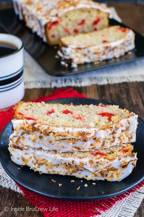 Two slices of tropical banana bread on a black plate with the glaze and coconut facing forward