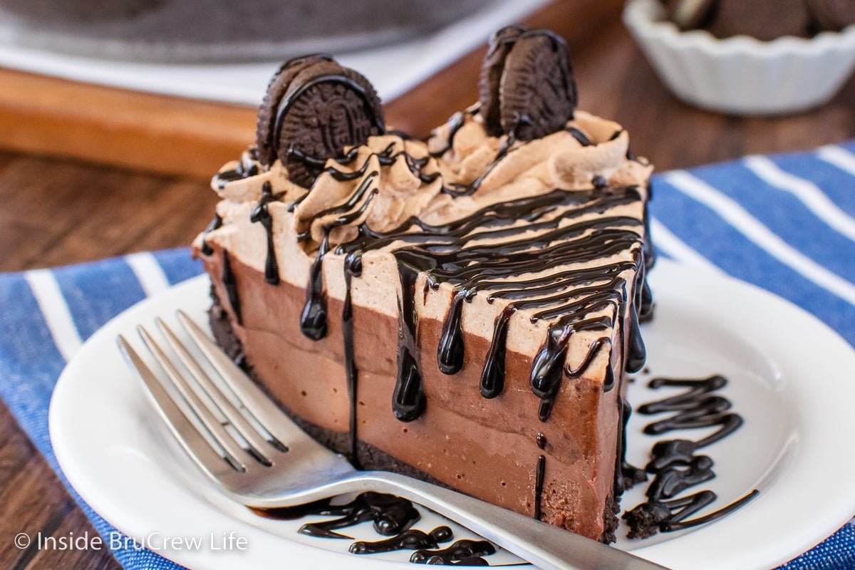 A white plate with a slice of chocolate pie topped with hot fudge and Oreos.