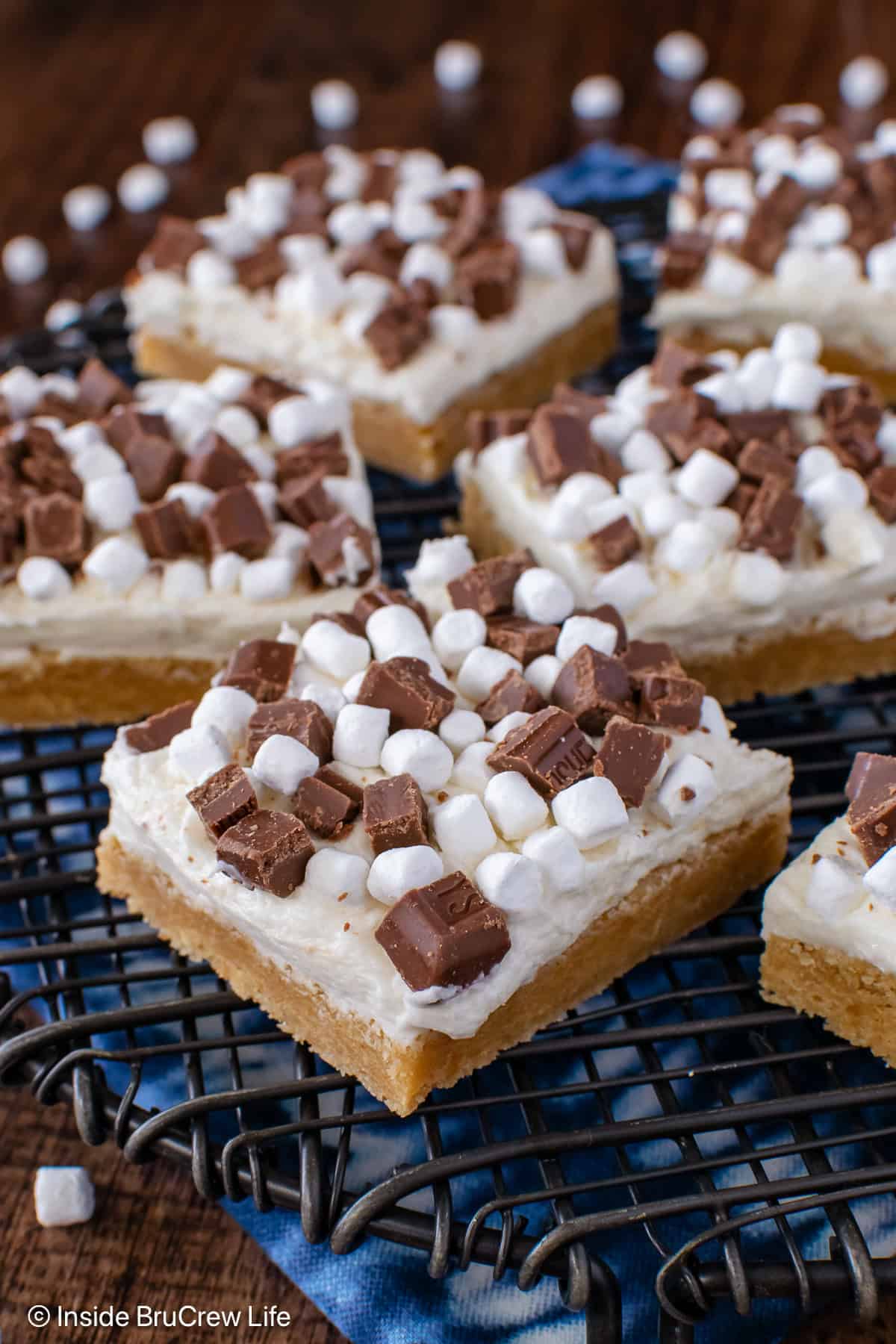 A close up of frosted s'mores cookie bars with candy and marshmallows on top.