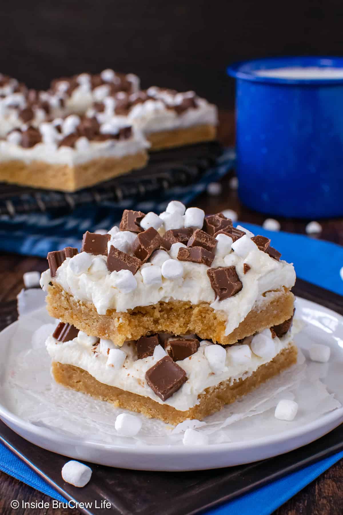 Two s'mores cookie bars stacked on a white plate with a bite out of the top cookie.