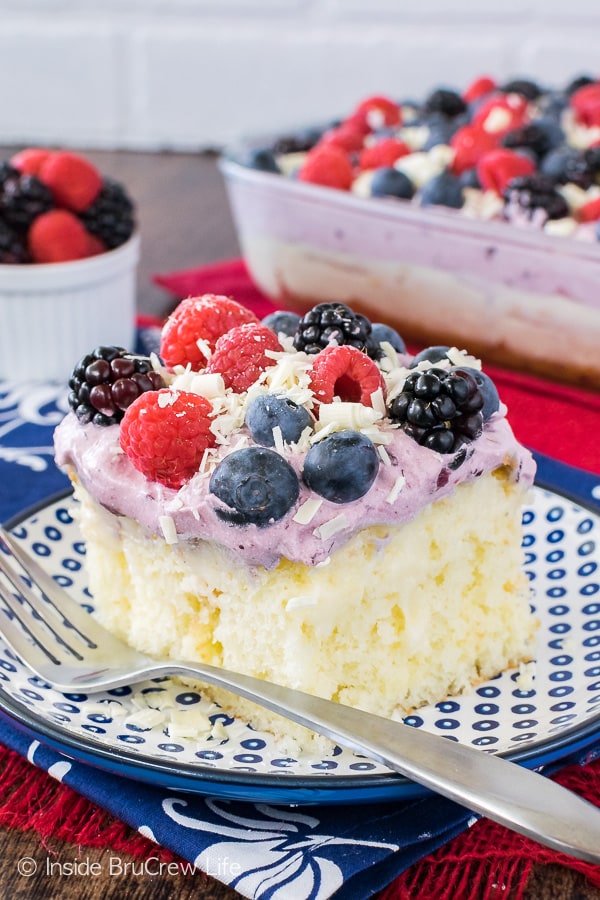 A square of white chocolate pudding cake topped with berry topping and fresh berries on a blue polkadot plate