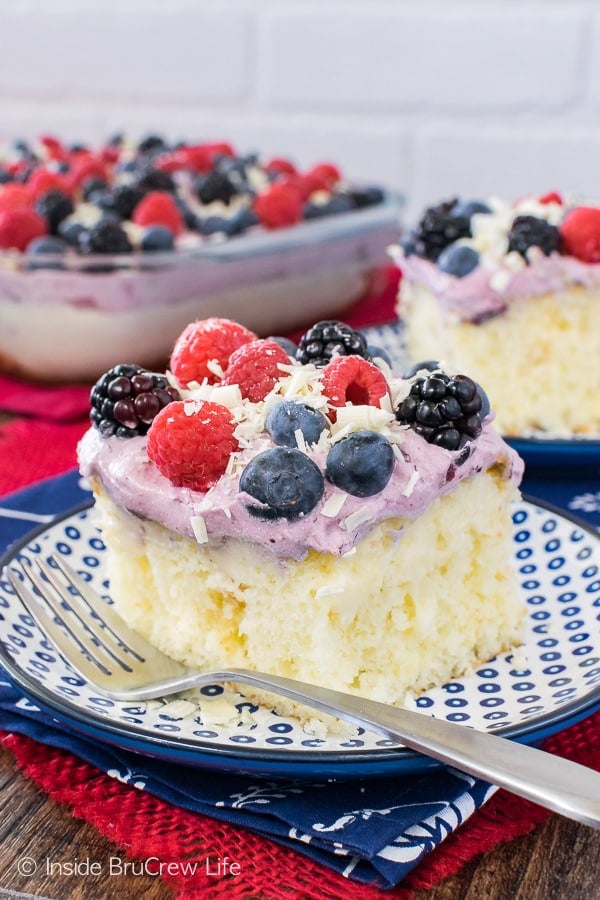 A square of white chocolate berry pudding cake topped with berry topping and fresh berries on a blue and white plate