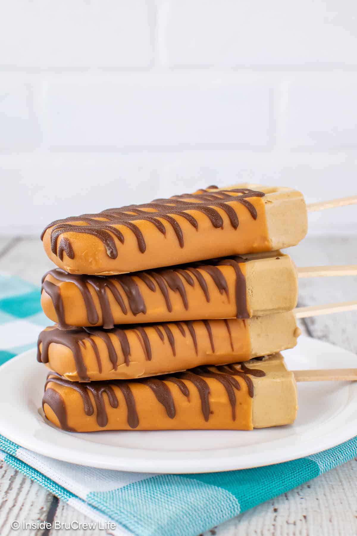 A stack of caramel dipped popsicles on a white plate.