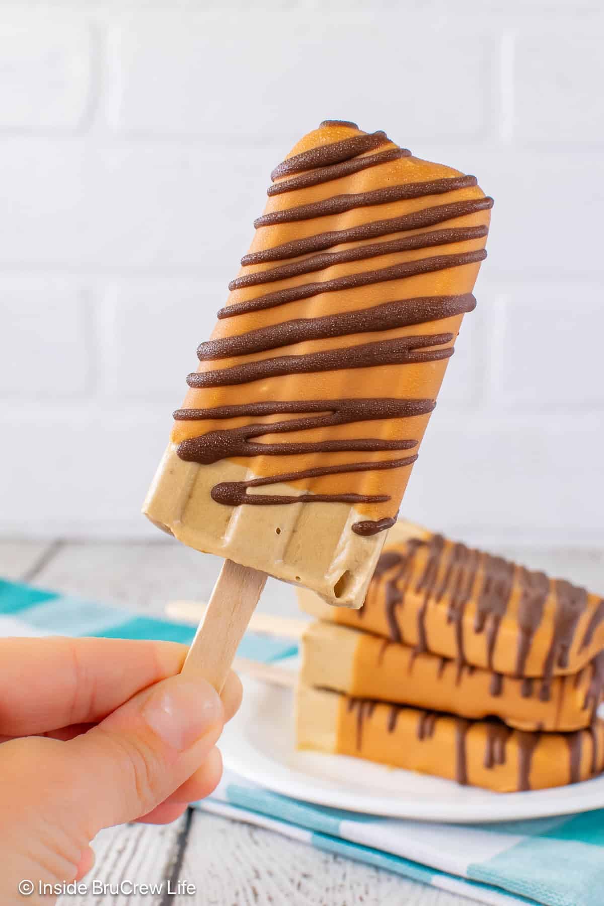 A coffee pudding pop with a caramel shell and chocolate drizzles held in the air.