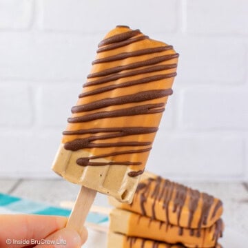 A coffee pudding pop with a caramel shell and chocolate drizzles held in the air.