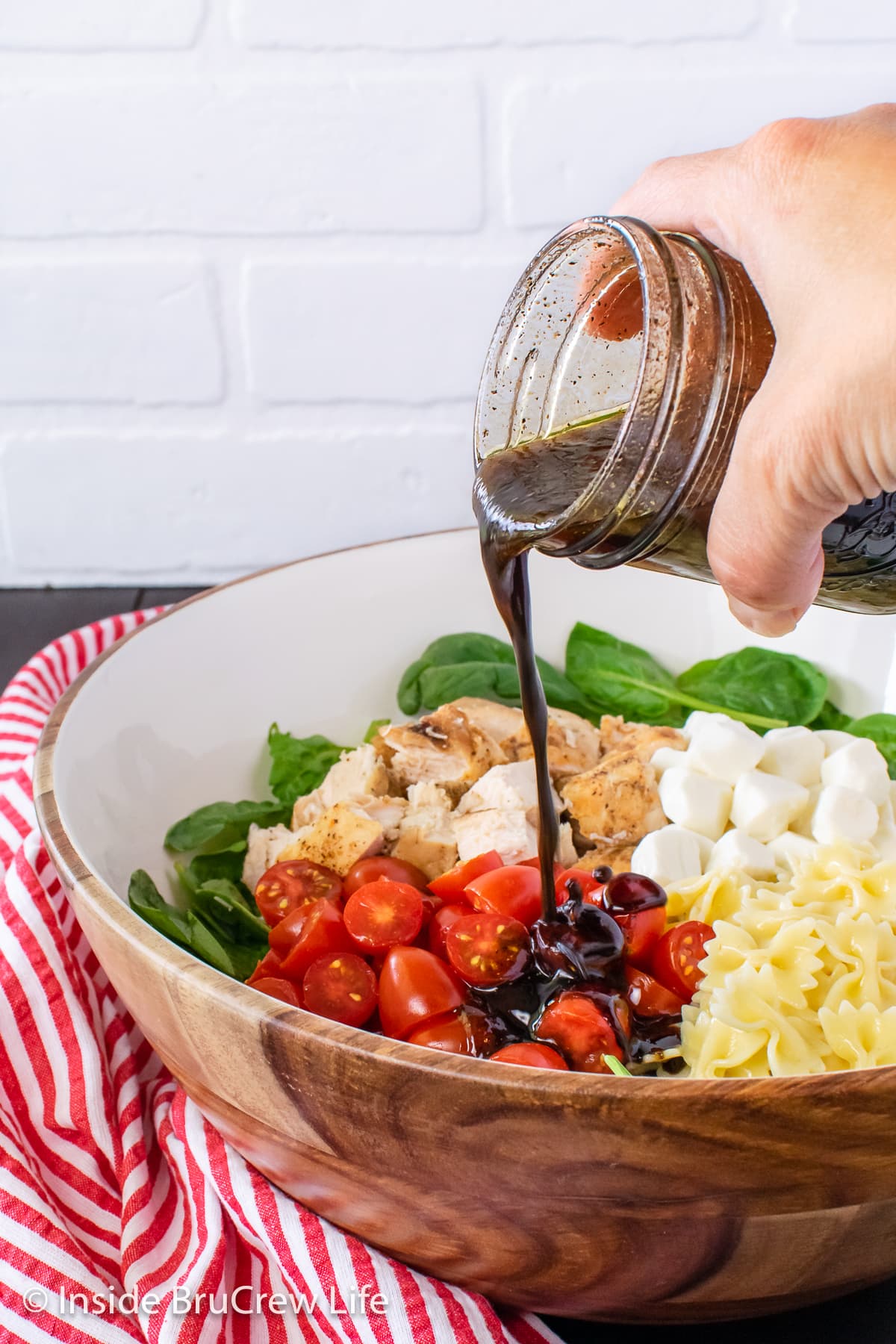 A bowl of salad ingredients with salad dressing being poured on top.