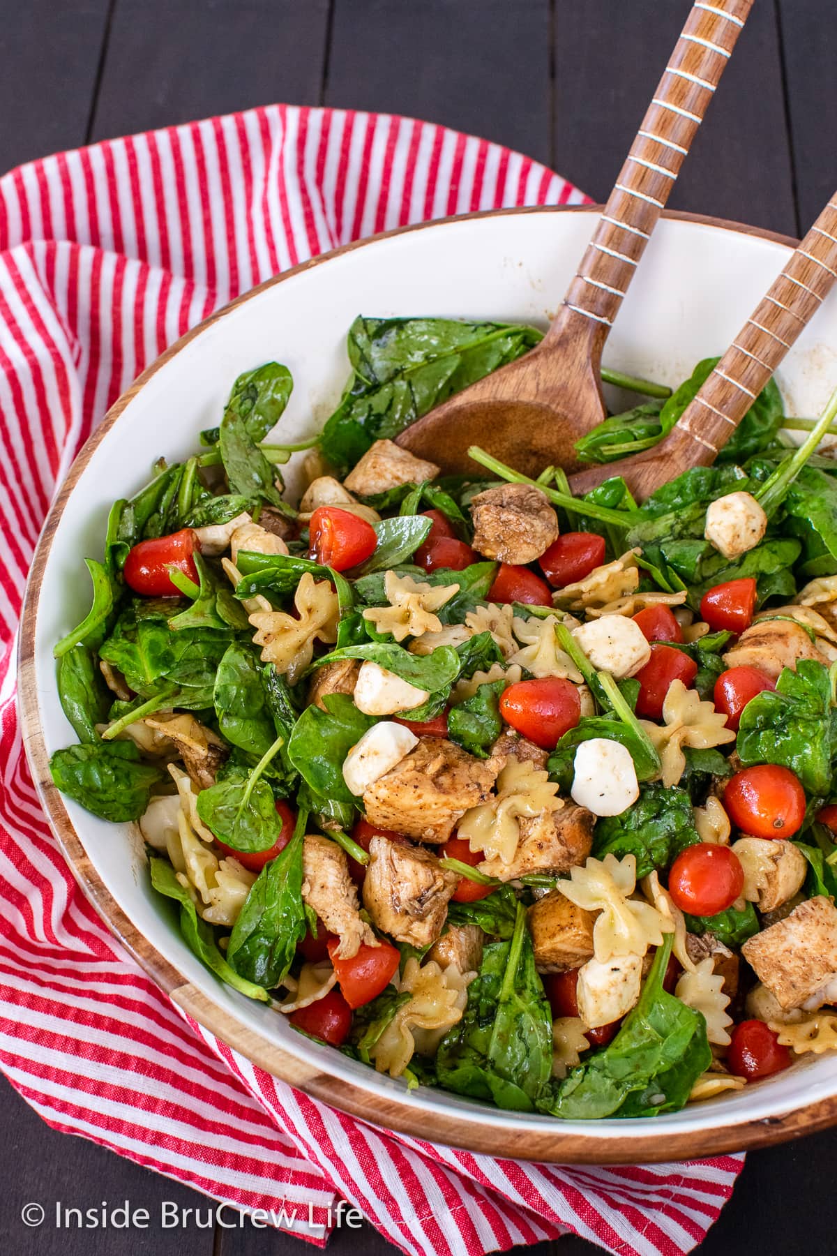 A bowl of spinach salad with chicken, tomatoes, and cheese.