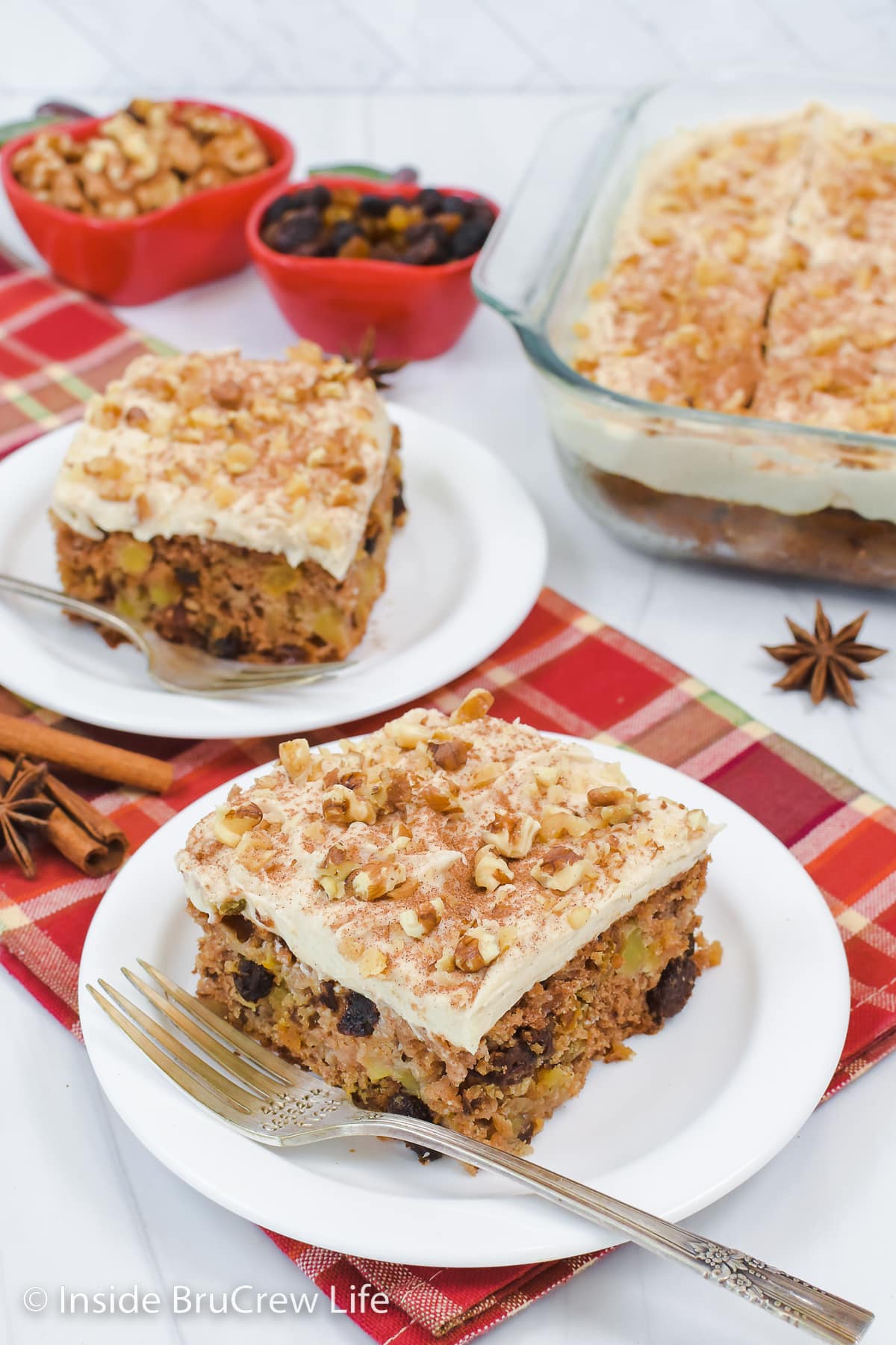 Two squares of frosted apple cake on white plates.