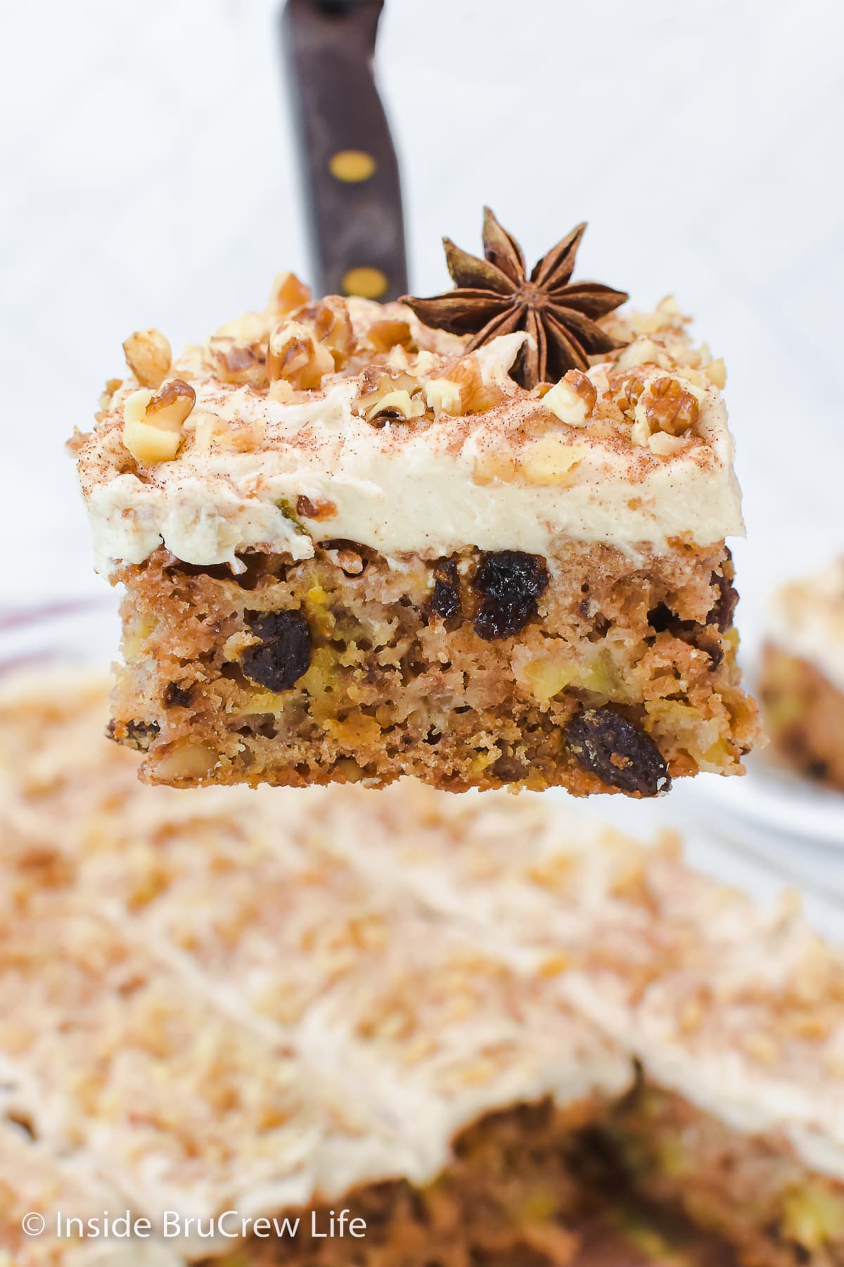 A square of apple cake with frosting being lifted out of a cake pan.