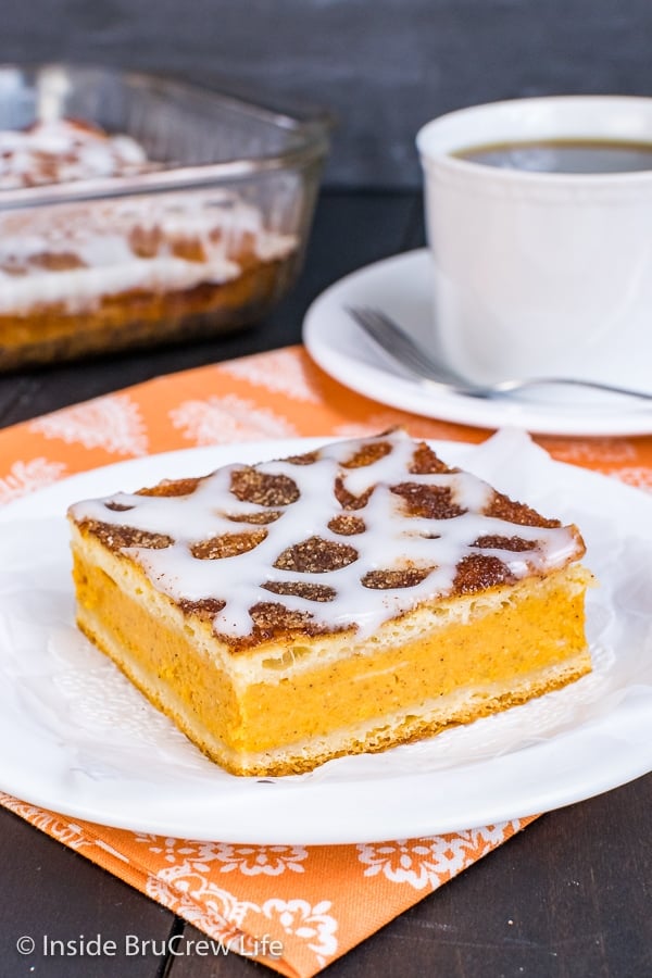 A white plate with a square of churro pumpkin pie cheesecake danish drizzled with a sweet glaze on it