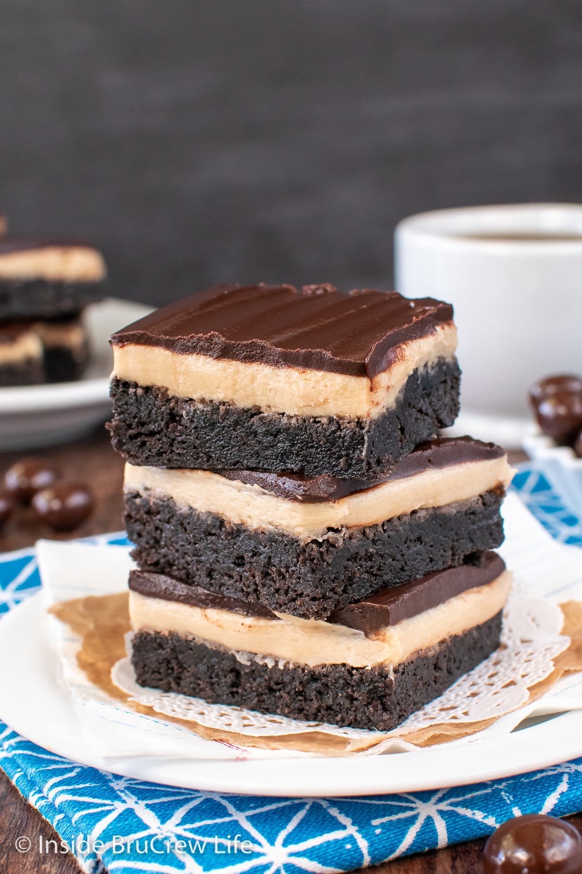 Three frosted brownies stacked on a white plate.