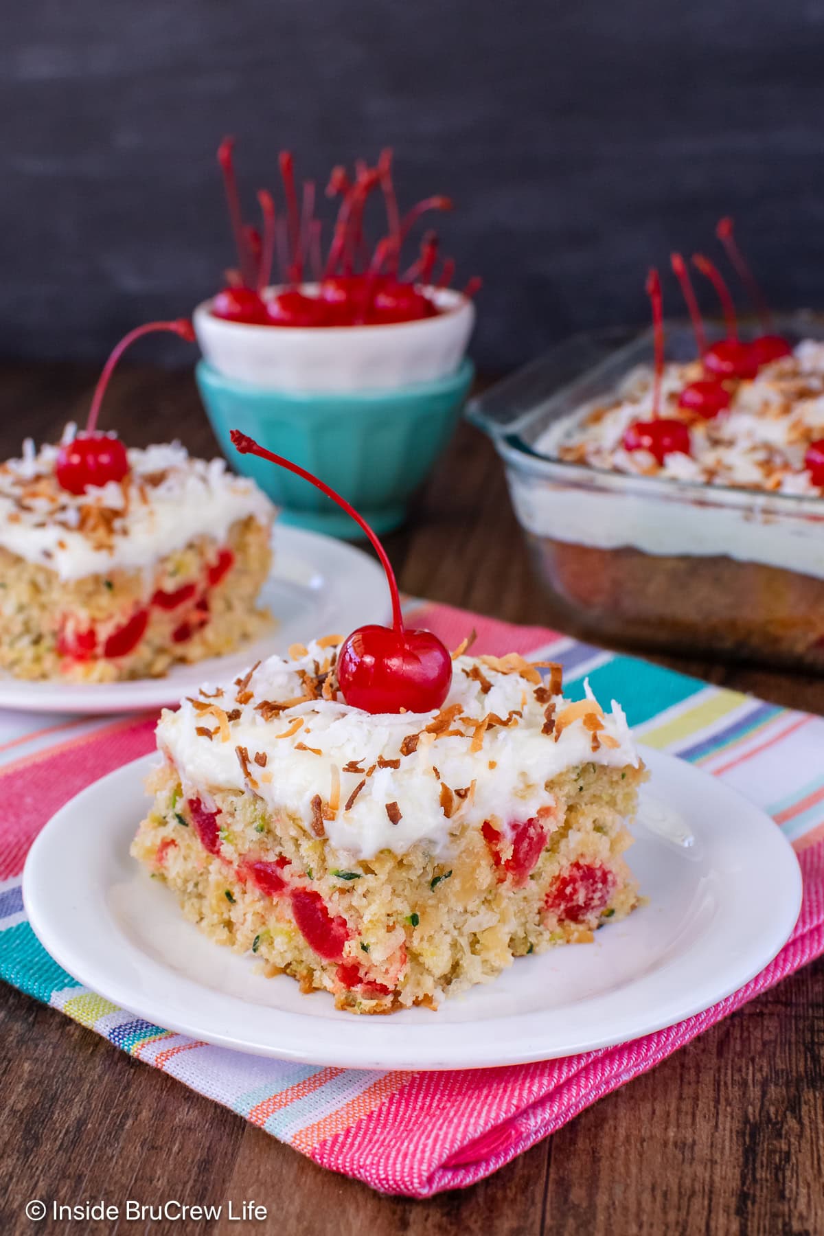 Zucchini cake topped with frosting and cherries on a white plate.