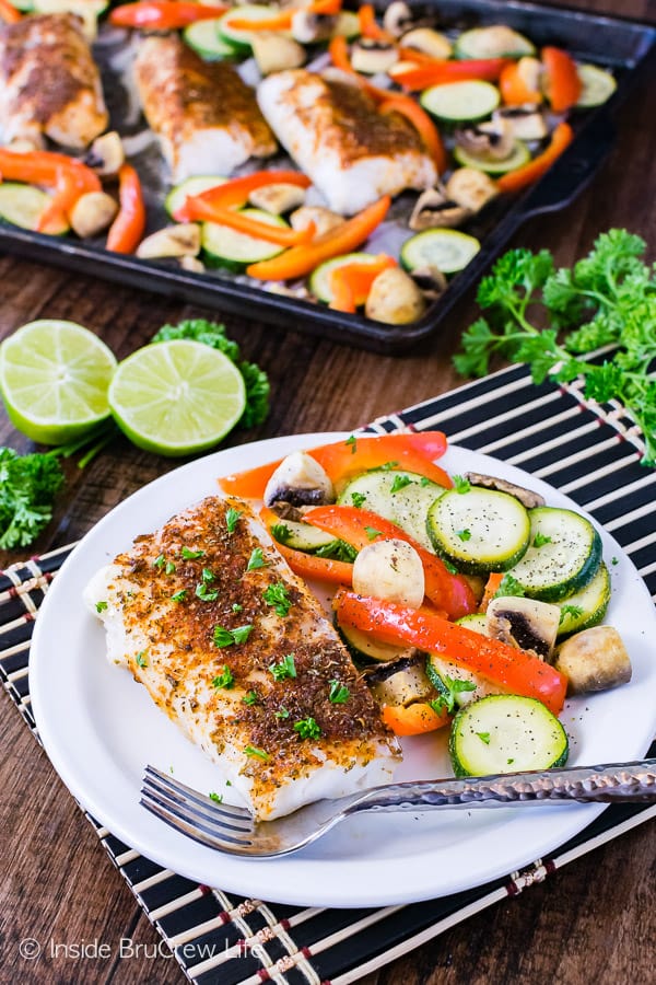 Overhead picture of a white plate with chili lime cod and roasted veggies and a sheet pan of more food