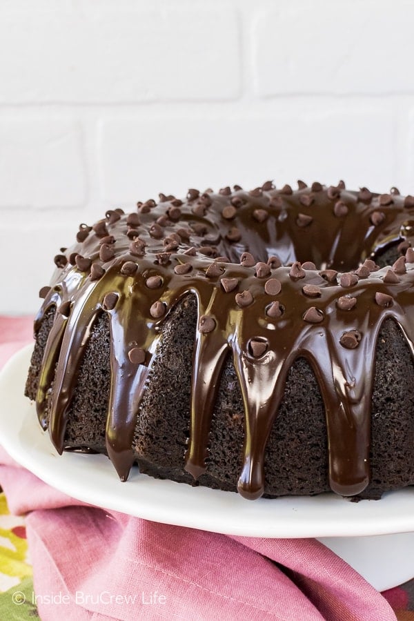 A close up of a chocolate zucchini bundt cake on a white cake plate.