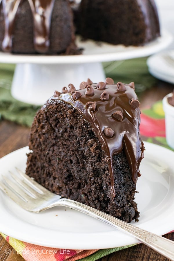 A white plate with a fork and a slice of chocolate zucchini bundt cake on it.