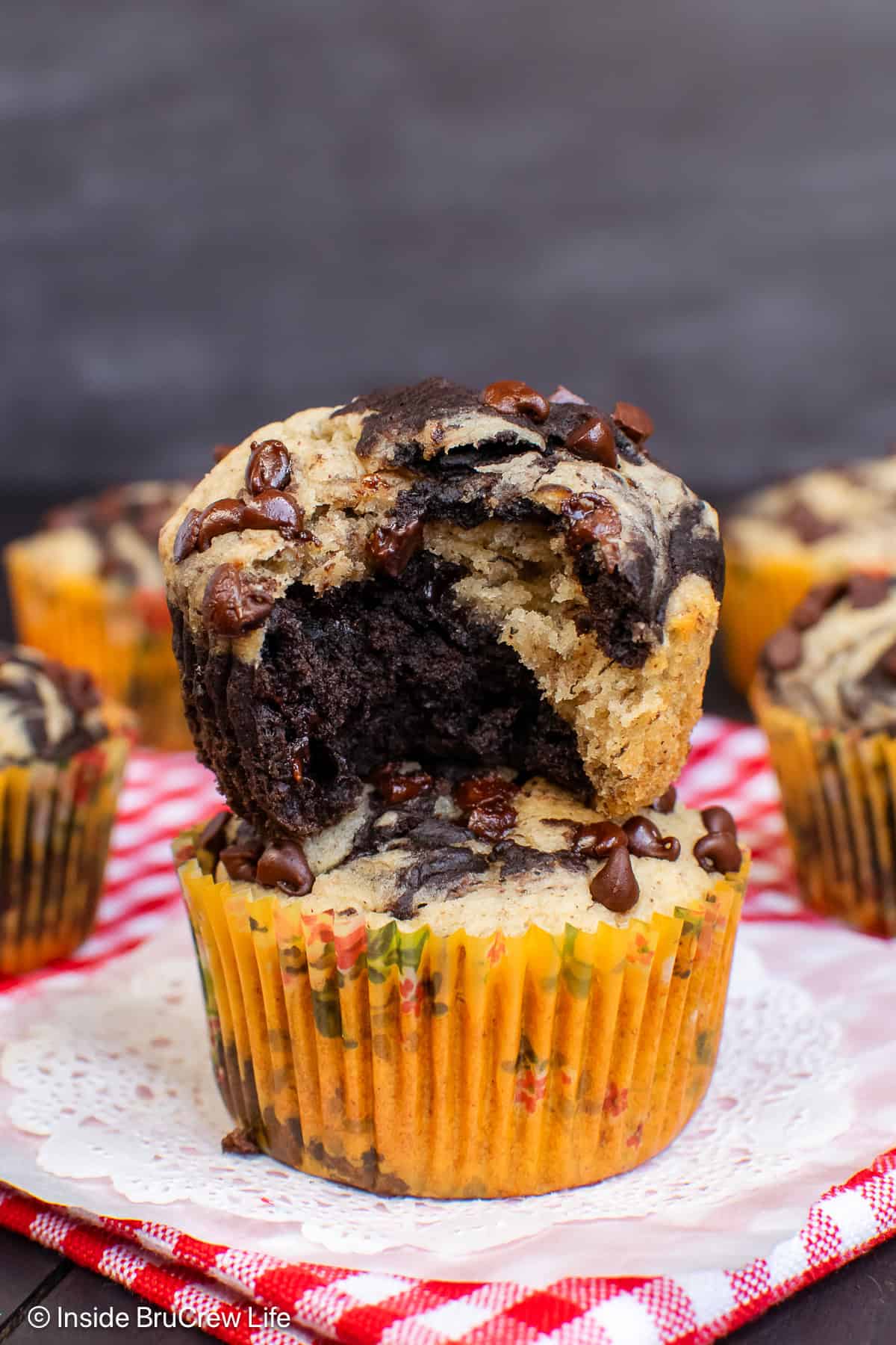Two chocolate banana marble muffins stacked on each other and bite out of the top one.