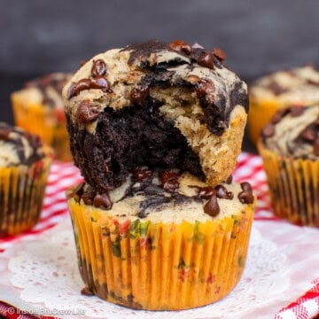 Two chocolate banana marble muffins stacked on each other and bite out of the top one.