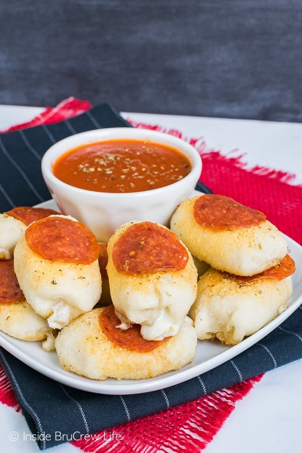 Stuffed pizza bites topped with pepperoni on a white plate with a bowl of pizza sauce.