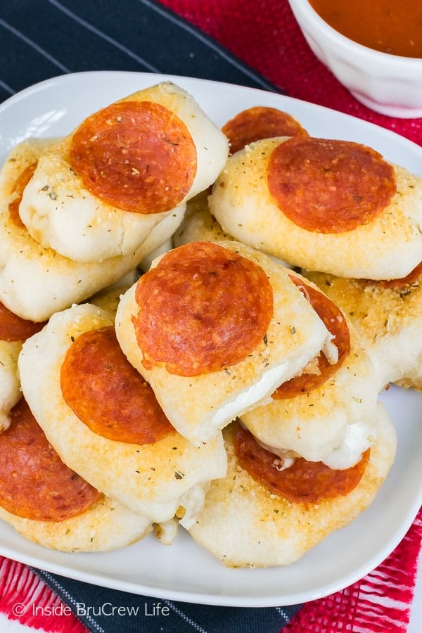 Overhead picture of pizza bites topped with pepperoni and seasonings on a white plate.