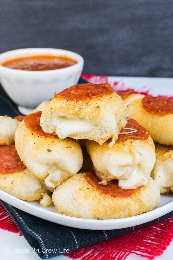 Stuffed pepperoni pizza bites stacked on a white plate with cheese oozing out of the ends.