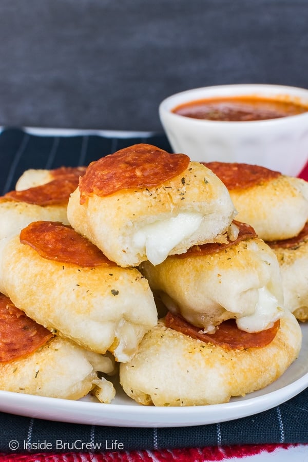 A white plate with stack of stuffed pizza bites with melted cheese coming out of the ends.