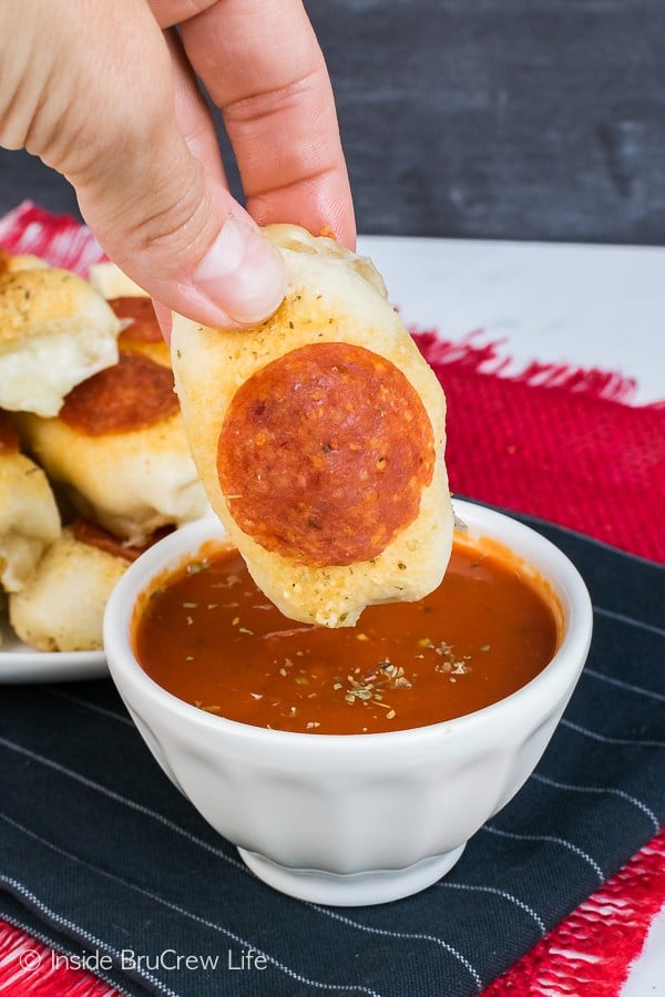 A white bowl of pizza sauce with a hand dipping a pizza bite into it.