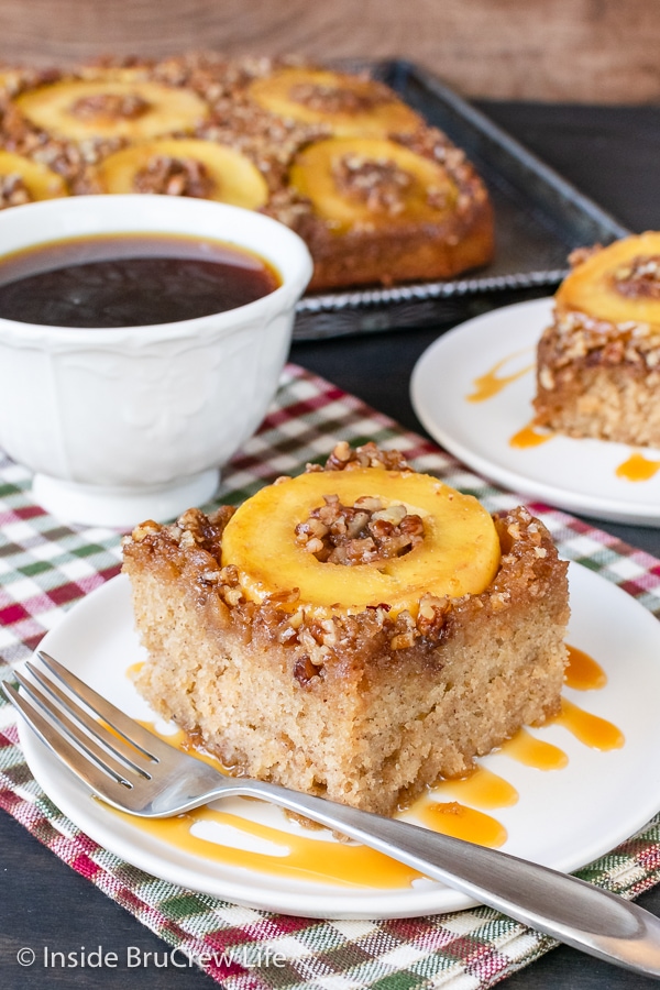 A white plate with a slice of apple upside down cake with caramel drizzles on it.